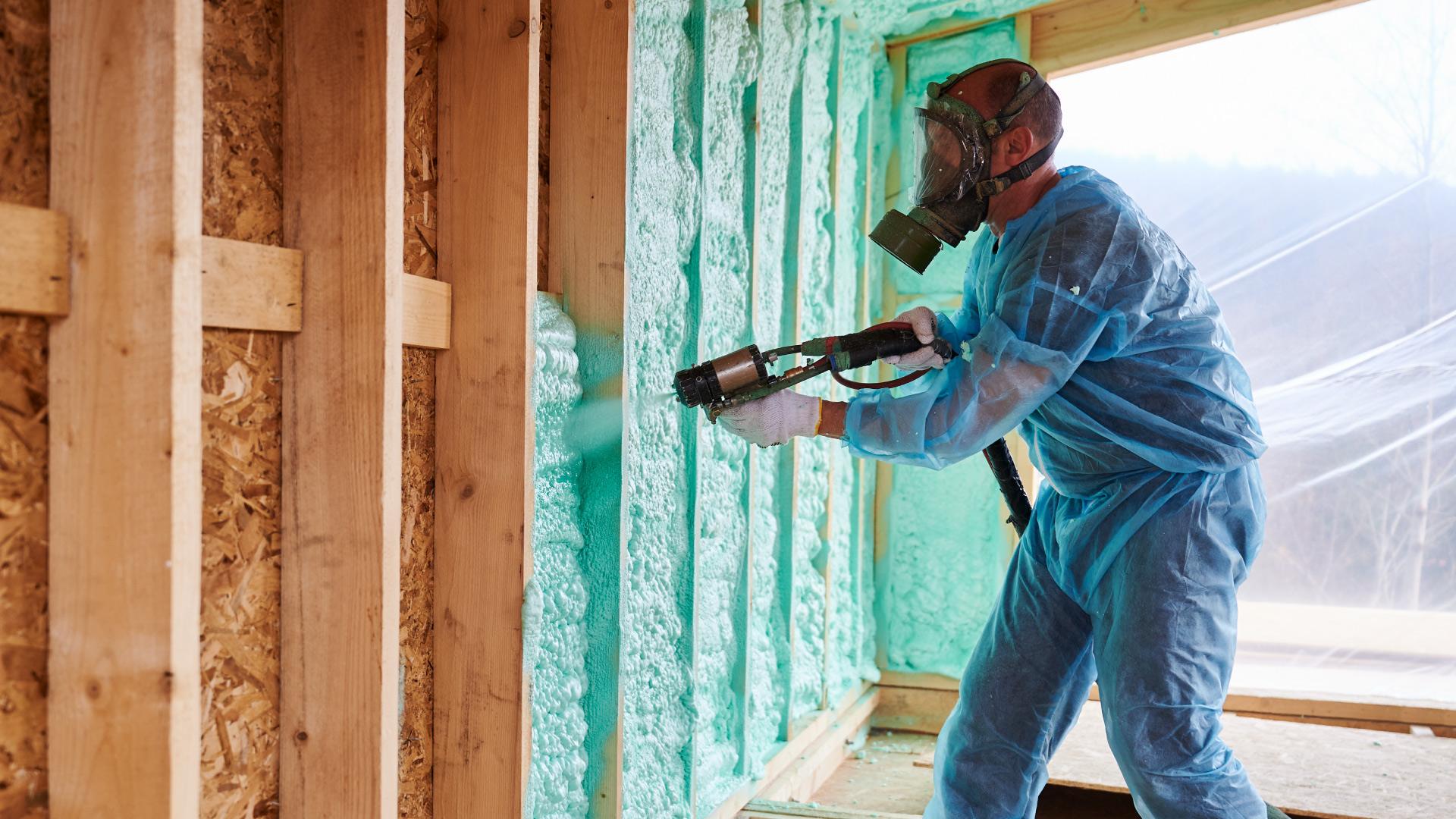 Spray foam repair in progress as a worker applies foam insulation to exposed framing.