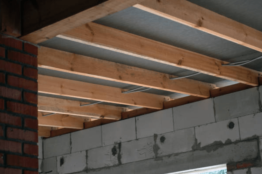 Exposed wooden ceiling joists and unfinished concrete block wall in a building under construction.