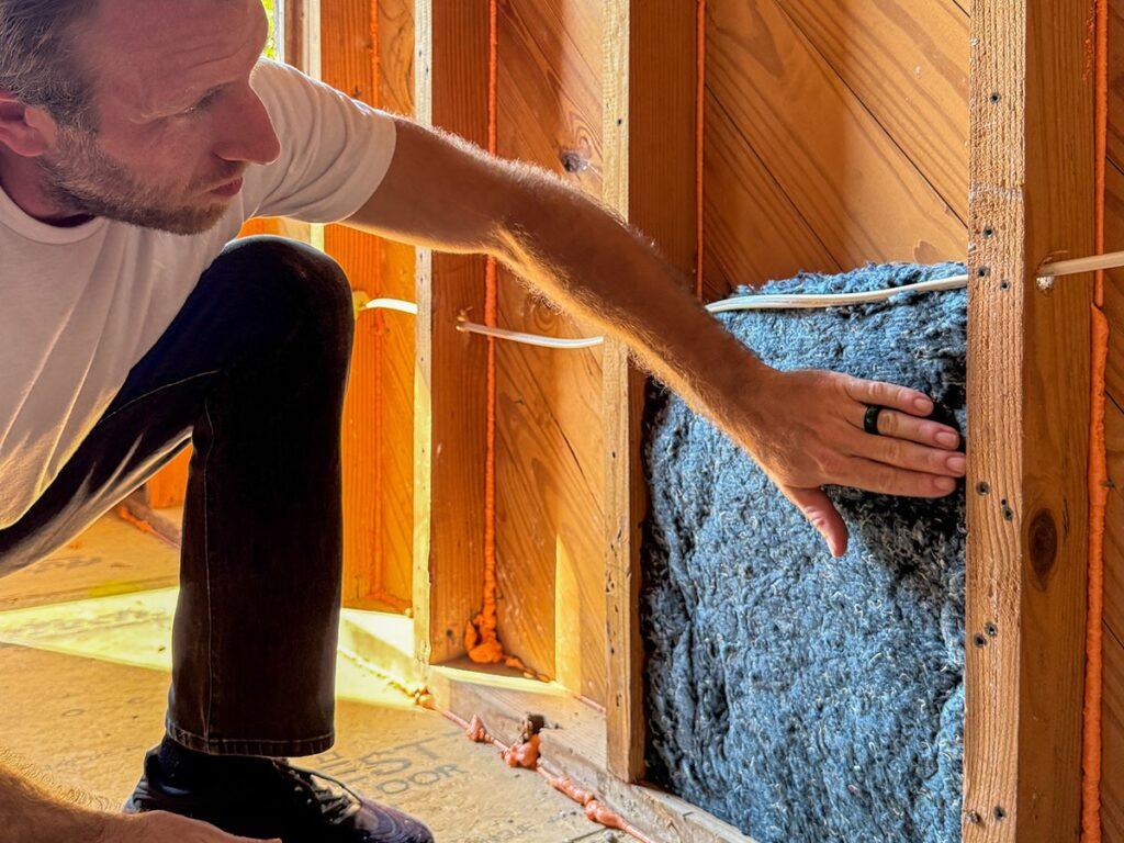 Worker installing a denim insulation panel into a wall frame.