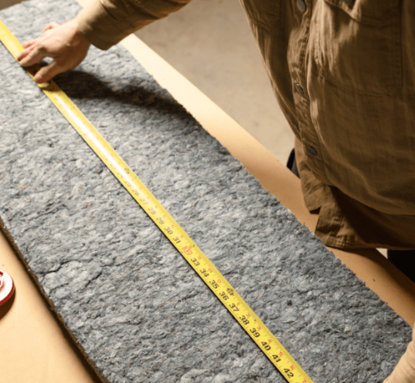 Hands measuring recycled cotton material to install denim insulation for soundproofing and thermal control.
