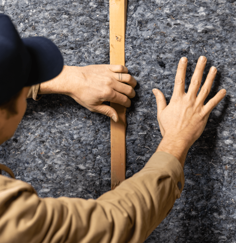 A worker safely installs denim insulation without gloves on. 