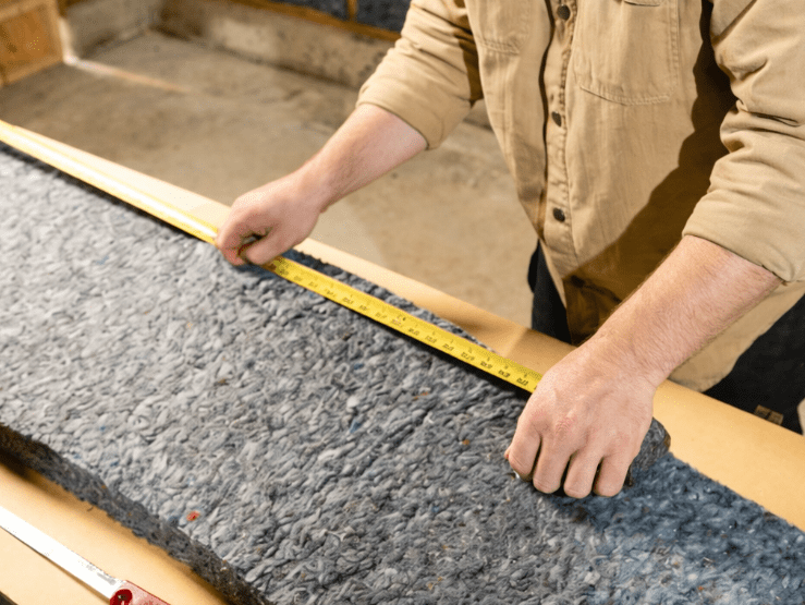 Worker using insulation tools to measure and cut denim insulation during installation.