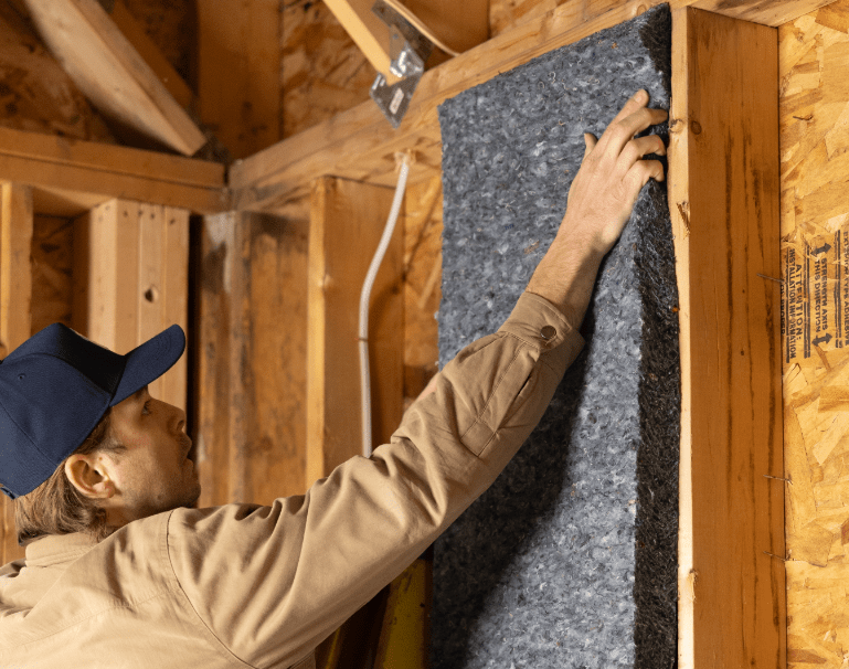 Worker installing recycled denim insulation between wall studs